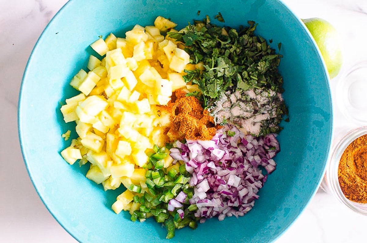 Diced pineapple, limes, cilantro, red onion, jalapeno in a bowl.