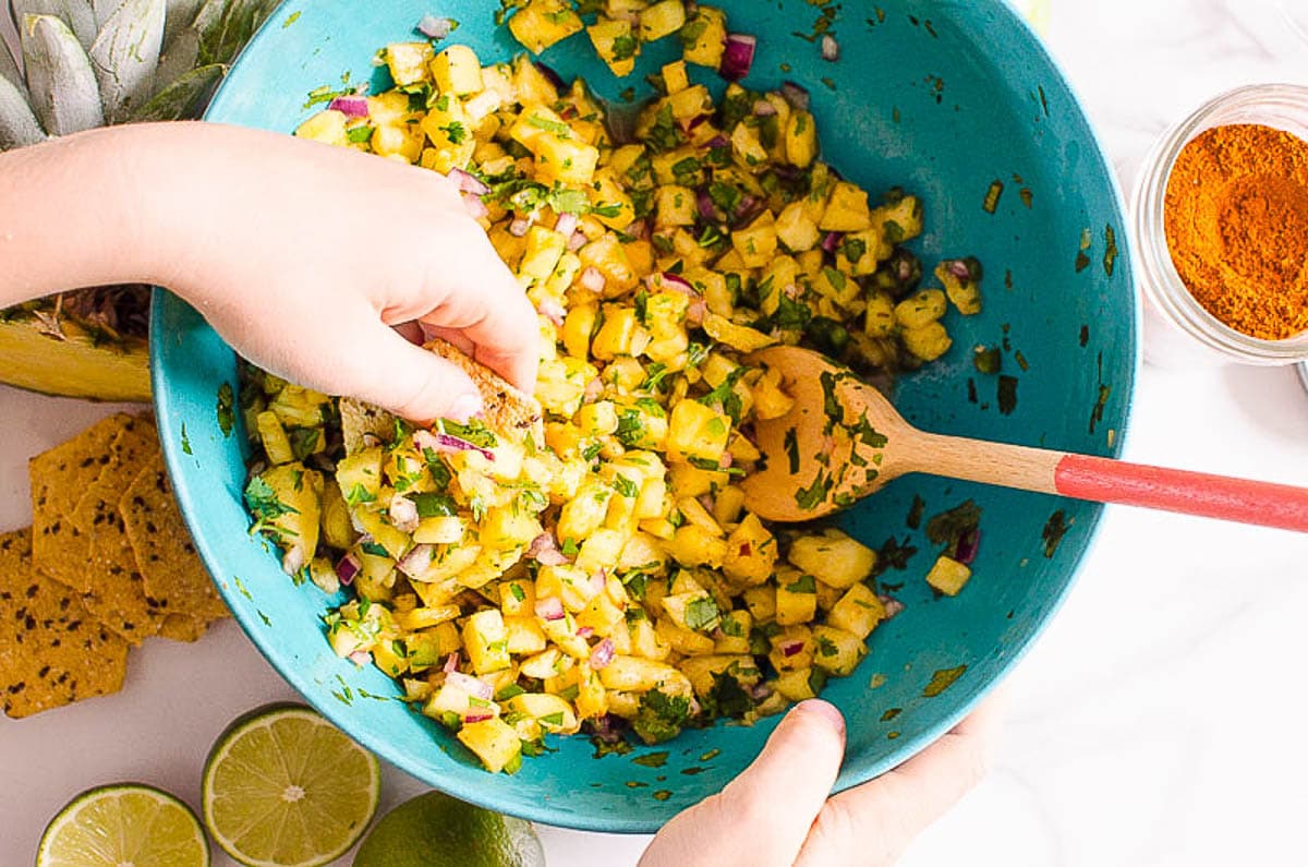 Hand scooping pineapple salsa with a chip from a bowl.