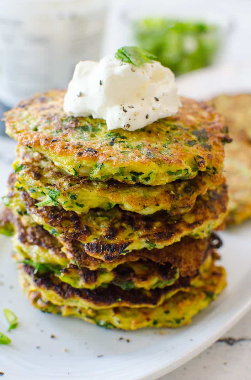 Zucchini Fritters stacked on plate with dollop of sour cream