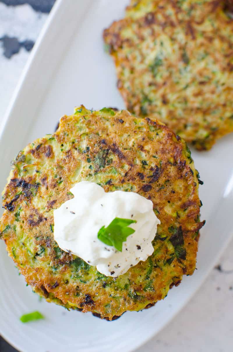Zucchini Fritters on white platter garnished with sour cream and parsley