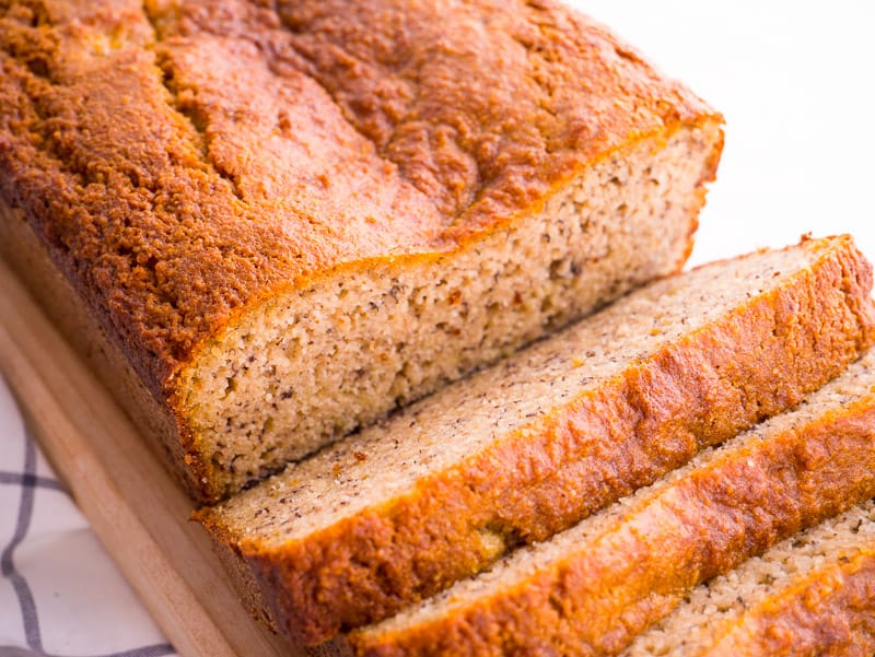 Loaf of almond flour banana bread partially sliced on wooden board.