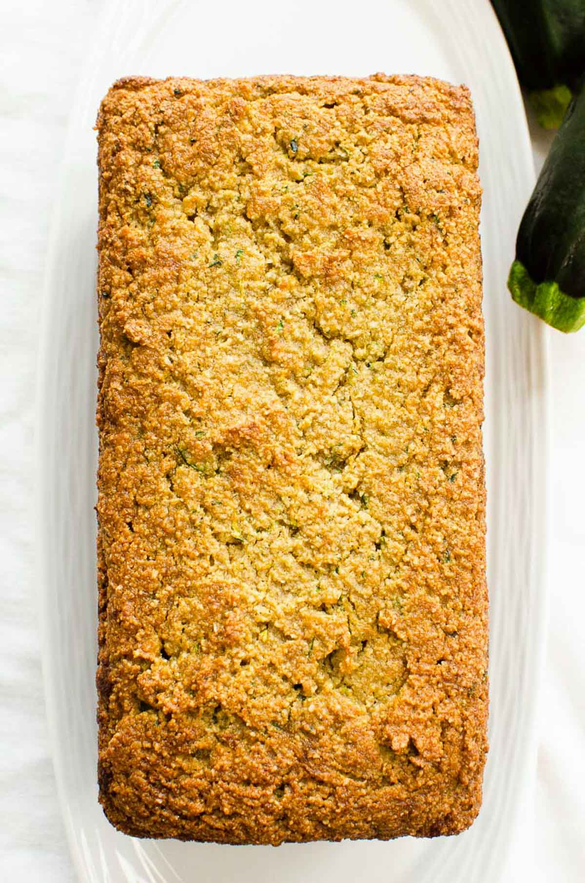 Almond flour zucchini loaf on white plate with fresh zucchini.