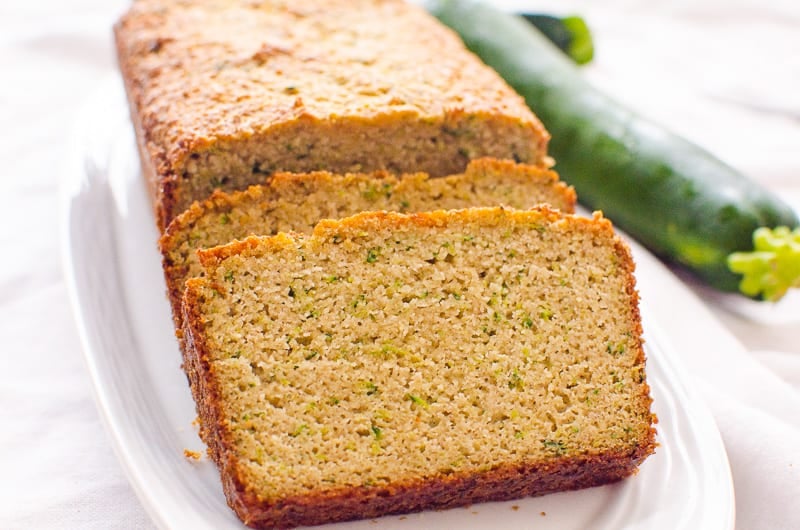 Almond flour zucchini bread sliced on white plate with a green zucchini beside the plate