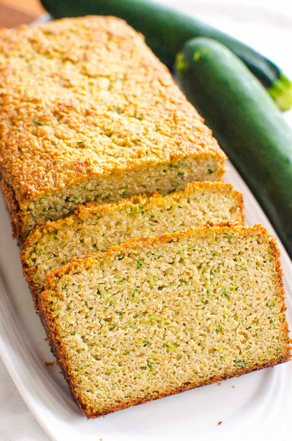 A loaf of almond flour zucchini bread with two slices on a white plate.