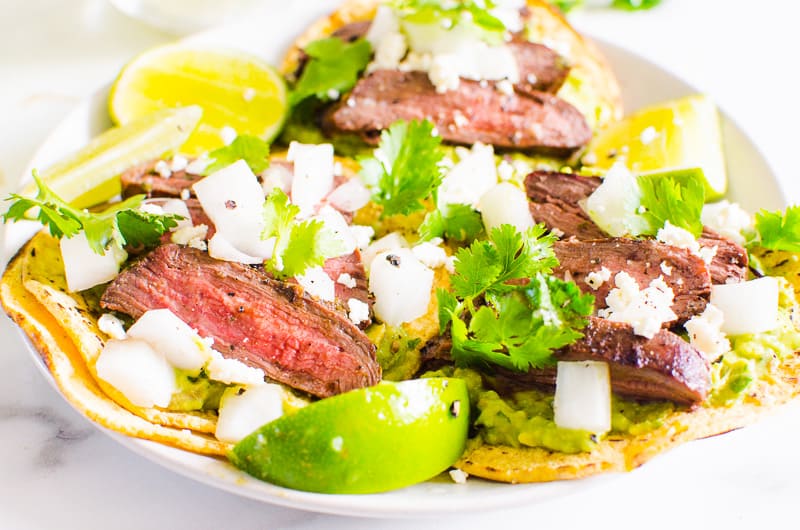 Carne Asada Tacos garnished with white onion, cilantro, cheese and lime