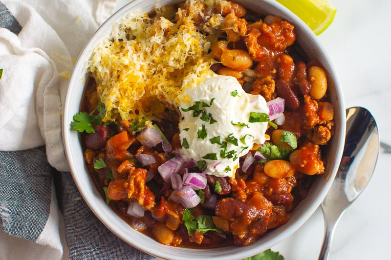 Slow cooker turkey chili in a bowl with Greek yogurt, onion, cheese and cilantro.