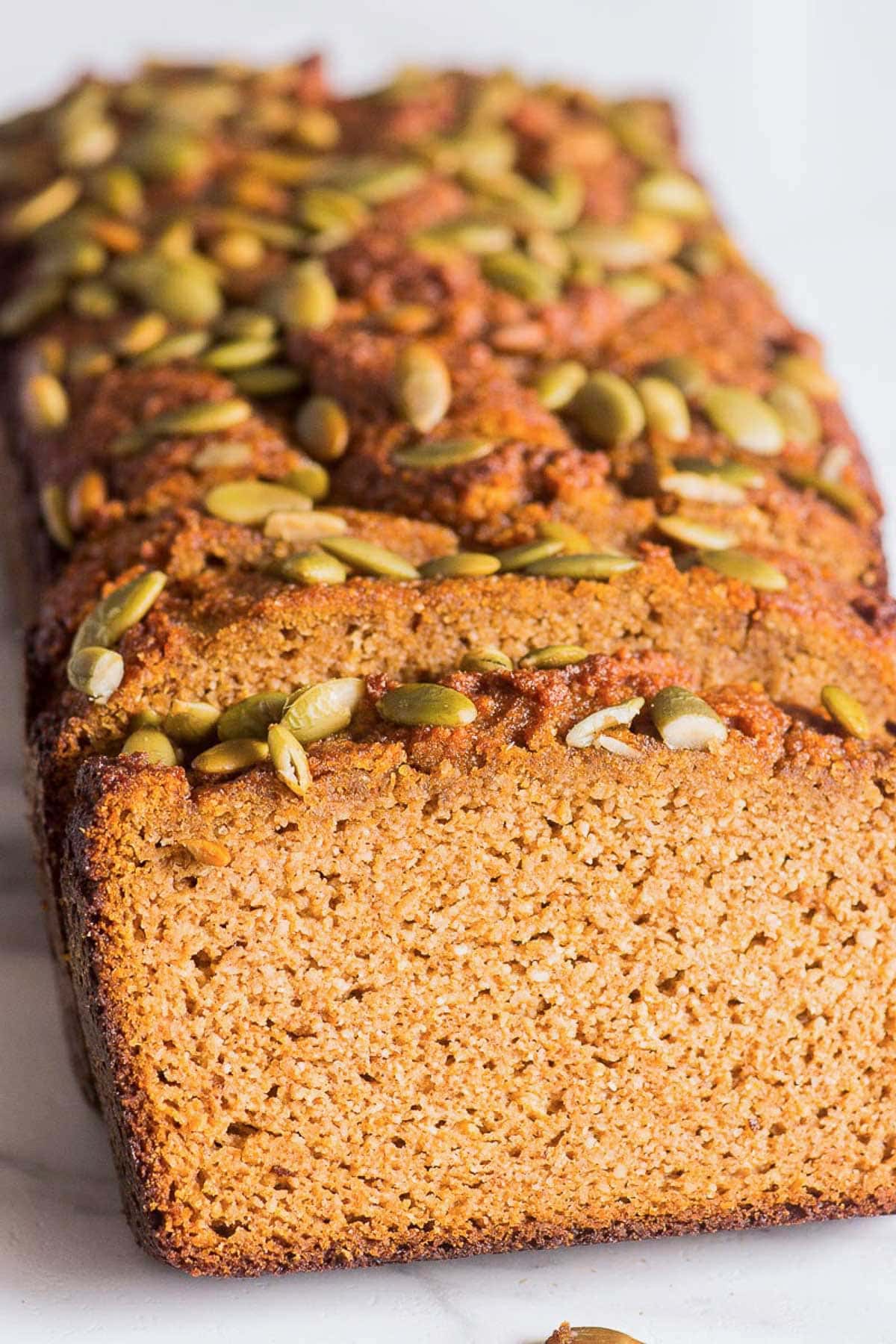 Sliced almond flour pumpkin bread topped with pumpkin seeds. 