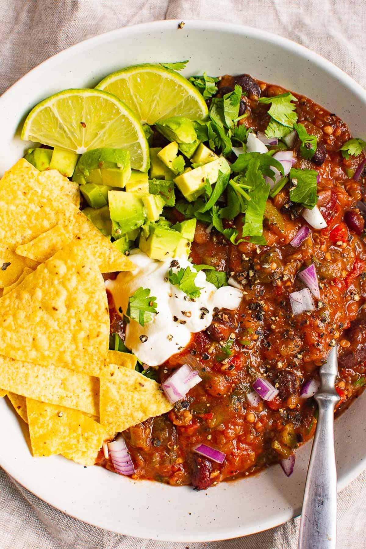Instant Pot vegetarian chili in a bowl topped with avocado, cilantro, lime and tortilla chips. 
