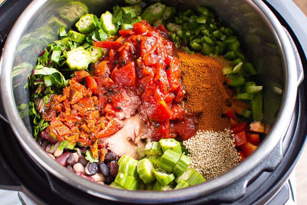 Bell peppers, chipotle peppers, quinoa, okra, beet leaves, beans and spices in inner pot of pressure cooker.