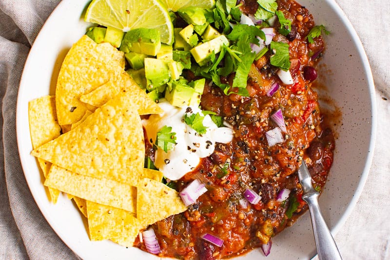 Chili with tortilla chips, lime slices, chopped red onion, cilantro and avocado.