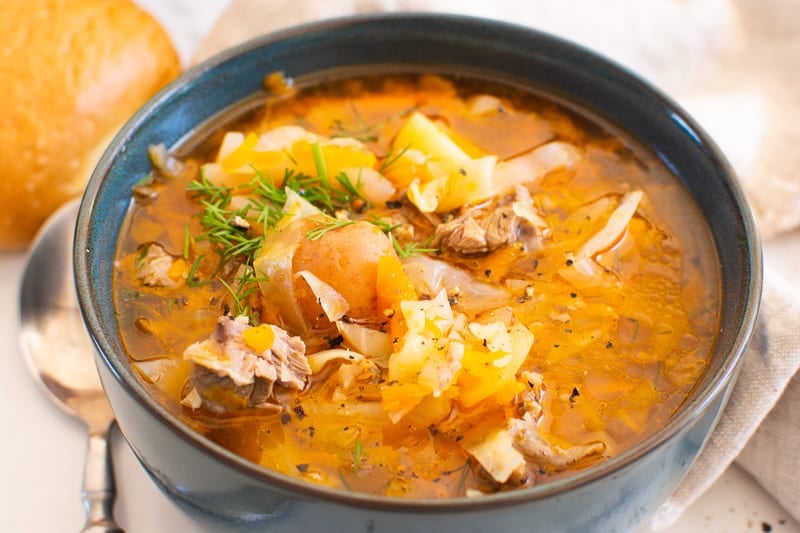 Russian cabbage soup with pork, potatoes and fresh dill served in a bowl with bread and spoon.