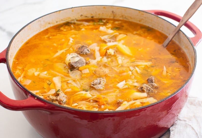 Russian cabbage soup in a large red pot with ladle. 