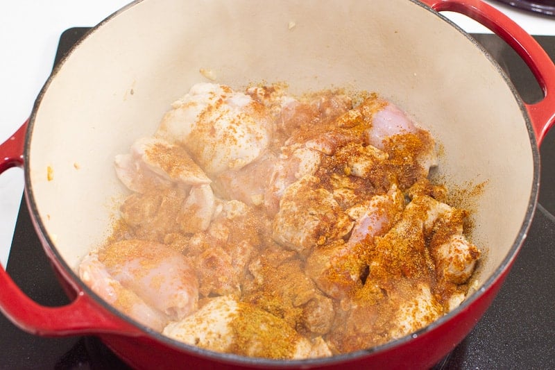 chicken thighs seasoned with spices cooking in red pot