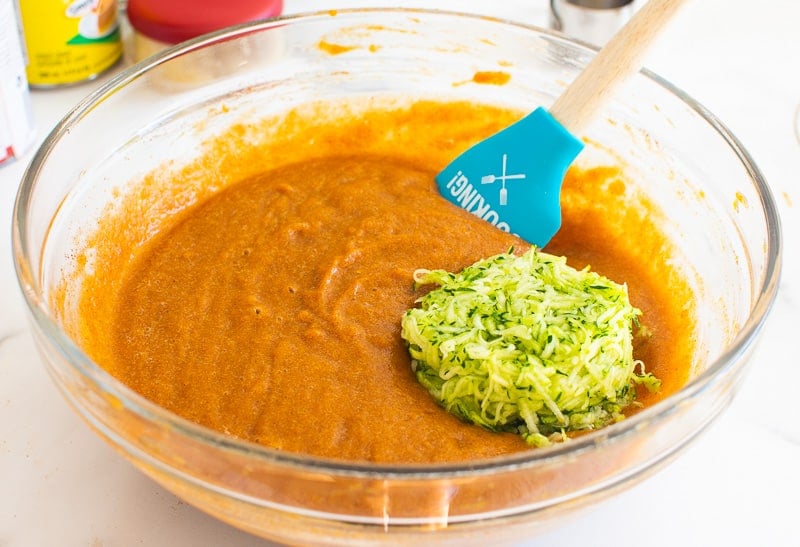 Pumpkin puree in a bowl with shredded zucchini being stirred in with spatula.