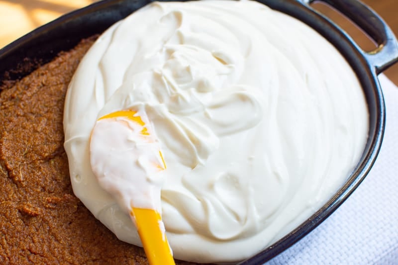 Frosting being spread on a cake with yellow spatula.