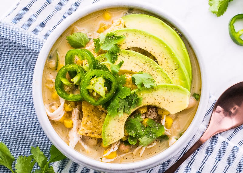 White chili in bowl with sliced avocado and jalapeno.