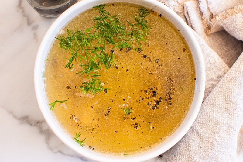 Instant Pot Chicken Bone Broth in white bowl garnished with dill and pepper