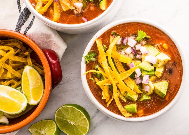 bows of instant pot chicken tortilla soup garnished with tortilla strips, red onion, cilantro and avocado