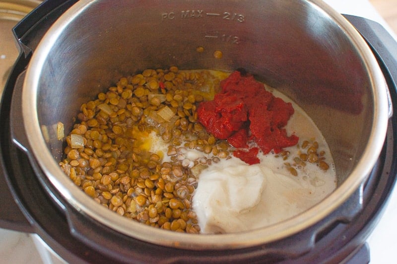 adding in coconut milk and tomato paste to lentil curry in the pressure cooker