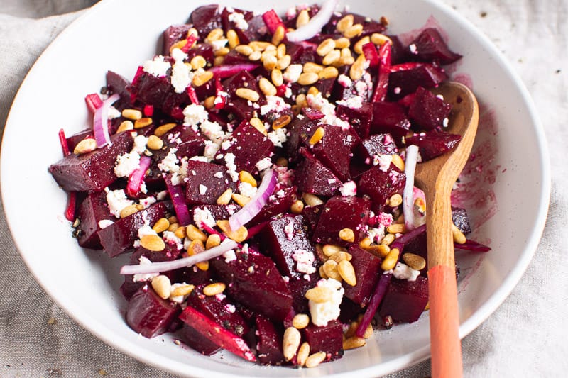 Beets in a bowl with pine nuts, cheese and red onion.