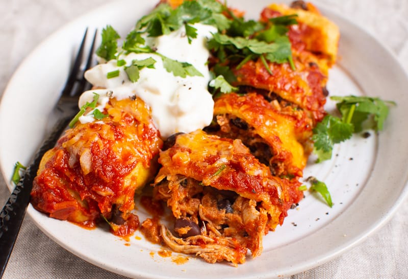 plate of chicken enchiladas served with sour cream and cilantro