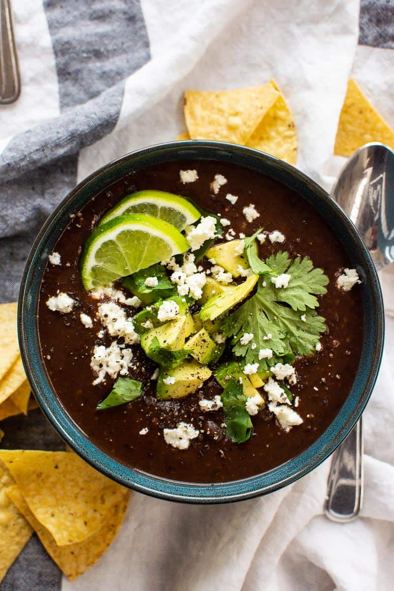 Instant Pot black bean soup with avocado, cilantro, lime and cheese in a bowl.