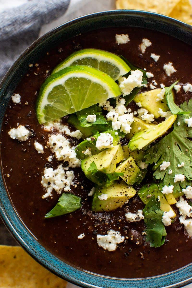 Instant Pot black bean soup in a bowl garnished with lime, cilantro and cheese.