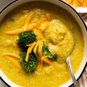 Healthy broccoli cheddar soup garnished with broccoli and cheese and served in a bowl with a spoon.