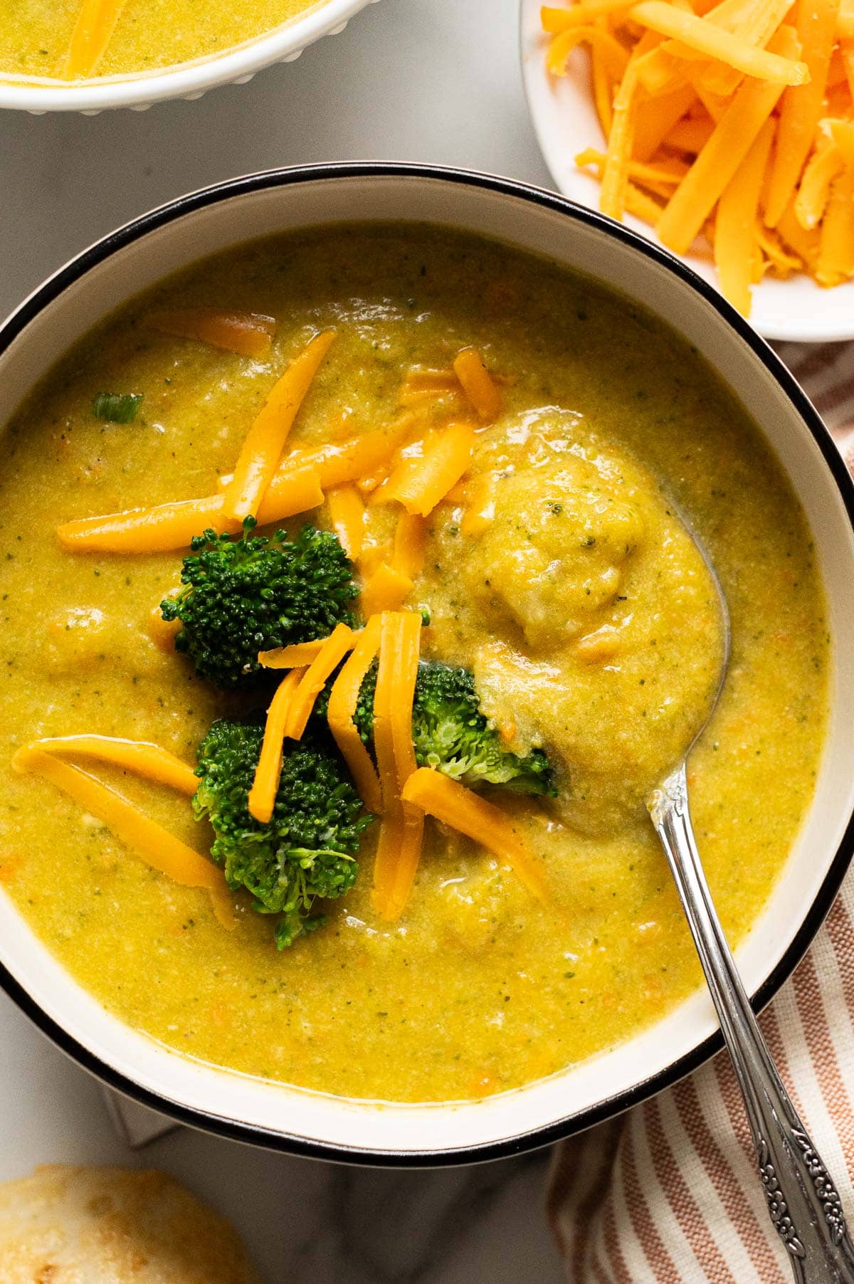 Healthy broccoli cheddar soup garnished with broccoli and cheese and served in a bowl with a spoon.