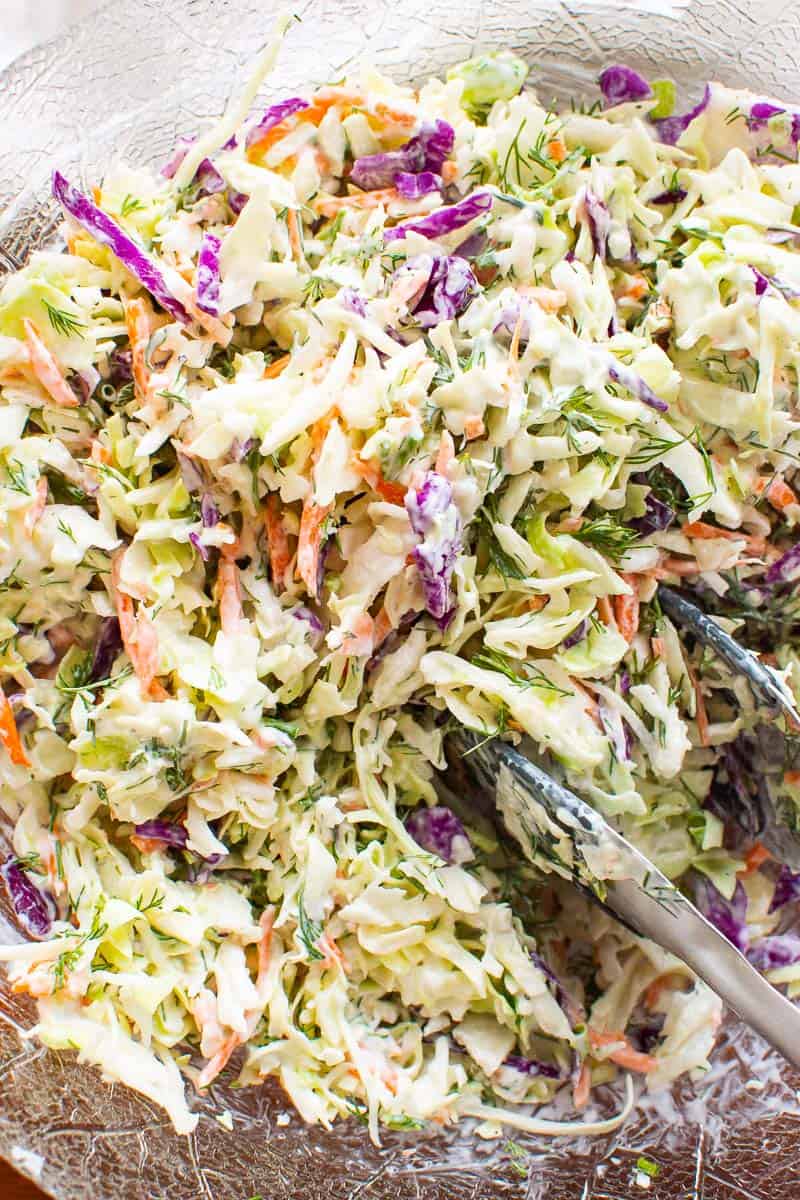 Healthy coleslaw with tongs in glass bowl.