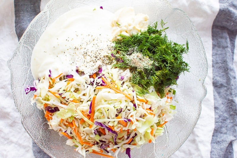 Coleslaw, dill, yogurt, mayo, salt and pepper in glass bowl. 