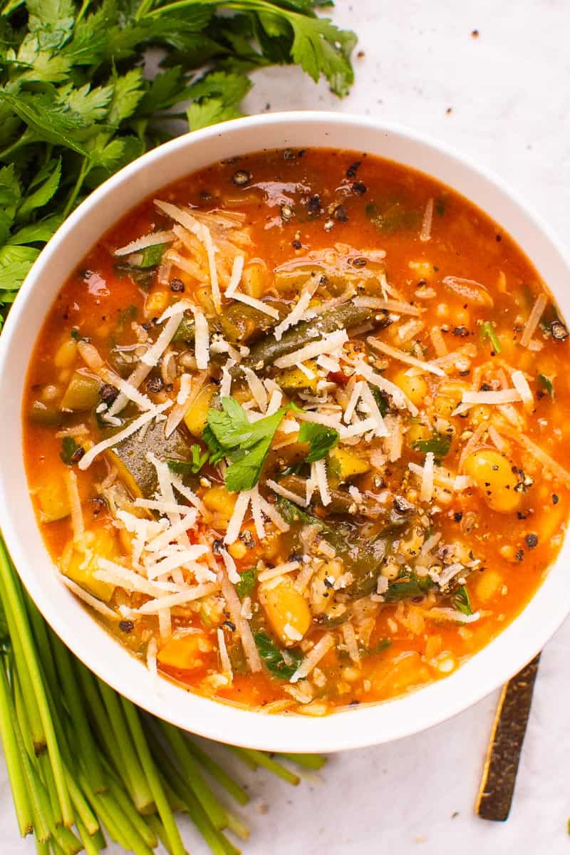 Minestrone soup in a bowl with fresh herbs beside the bowl.