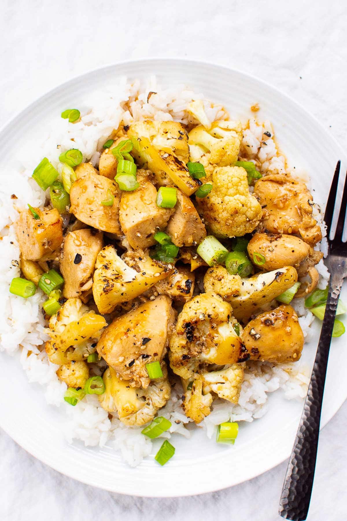 white dish of teriyaki chicken and cauliflower served over white rice with fork