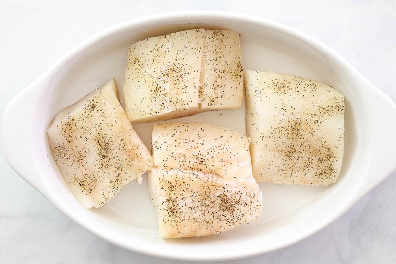 overhead image of seasoned cod fillets in a white baking dish