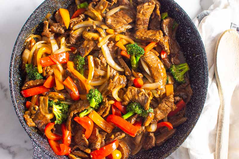 beef stir fry in a skillet and wooden spoon on towel