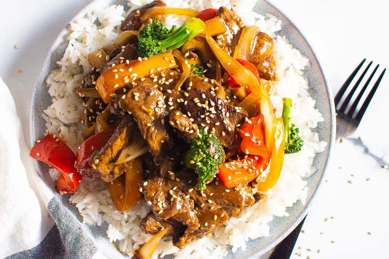 beef stir fry with rice and sesame seeds on a plate