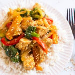 Healthy chicken stir fry garnished with sesame seeds and served over a bed of rice on a plate.
