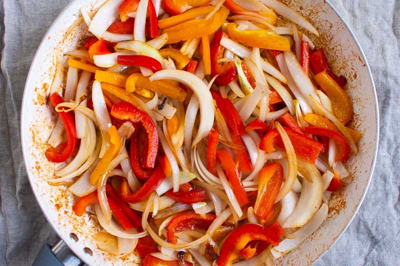 Cooked sliced onions and bell peppers in a skillet.