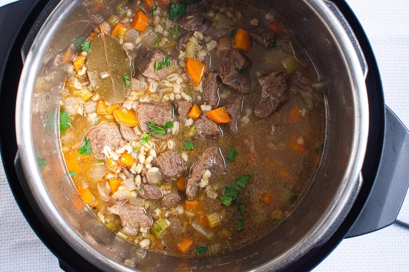 Instant Pot Beef Barley Soup in pressure cooker with bay leaf.