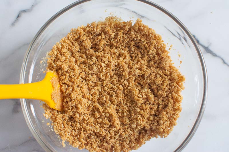 cheesecake crust crumbs in glass bowl and yellow spatula