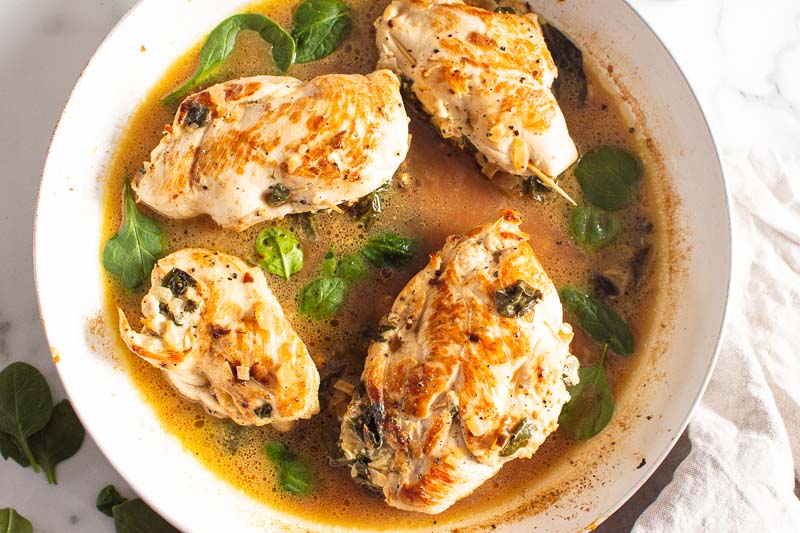 spinach stuffed chicken breast in white skillet with spinach