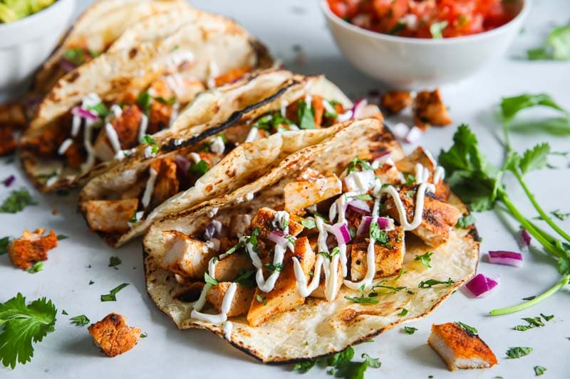 Closeup of Chicken Tacos with some cilantro and pico de gallo in the background.