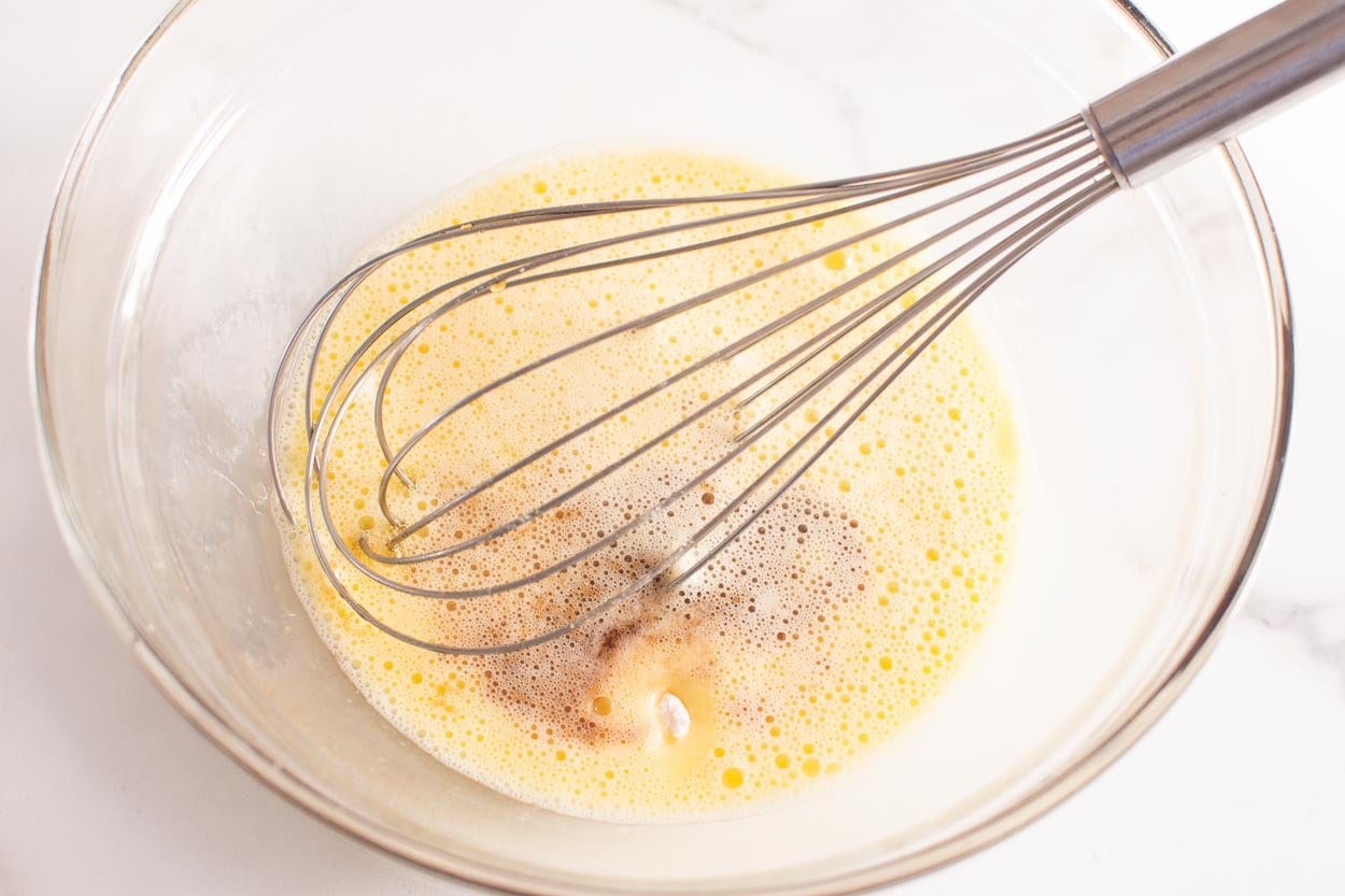 Maple syrup, eggs, baking essentials being whisked in glass bowl.