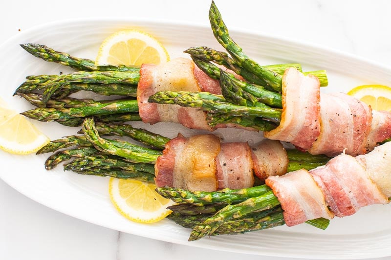 Asparagus wrapped in bacon on a plate with lemon.