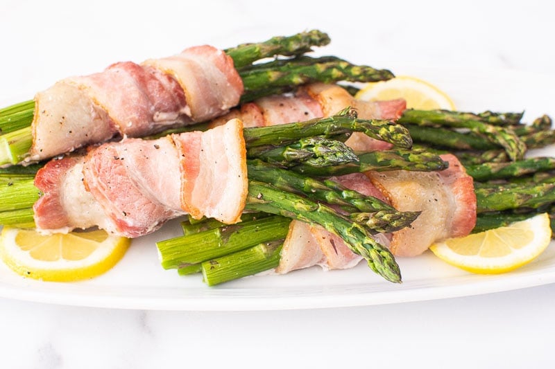 Bacon wrapped asparagus on serving plate with lemon.