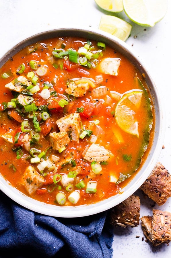 Salmon soup served with green onions and lime in a bowl with bread.