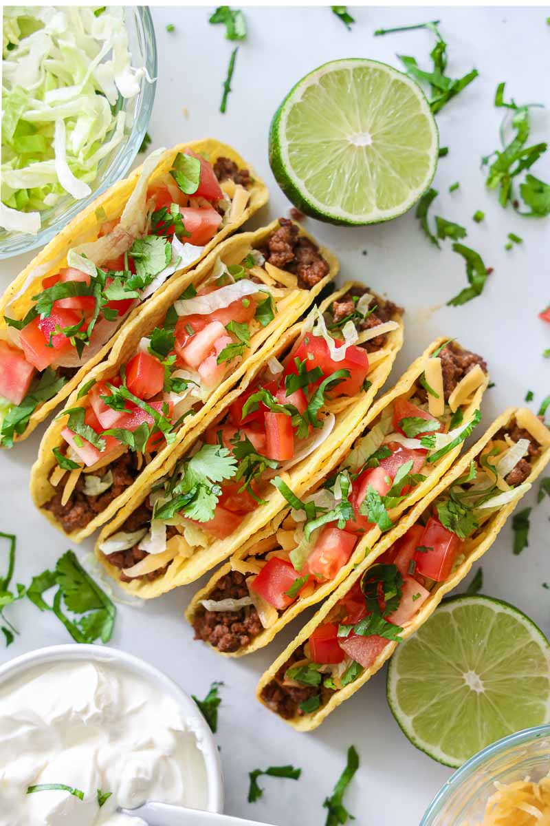 Overhead of Ground Beef Tacos with toppings and limes nearby