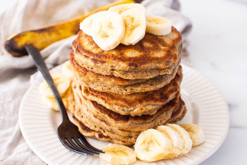 healthy banana pancakes served on white plate with sliced bananas