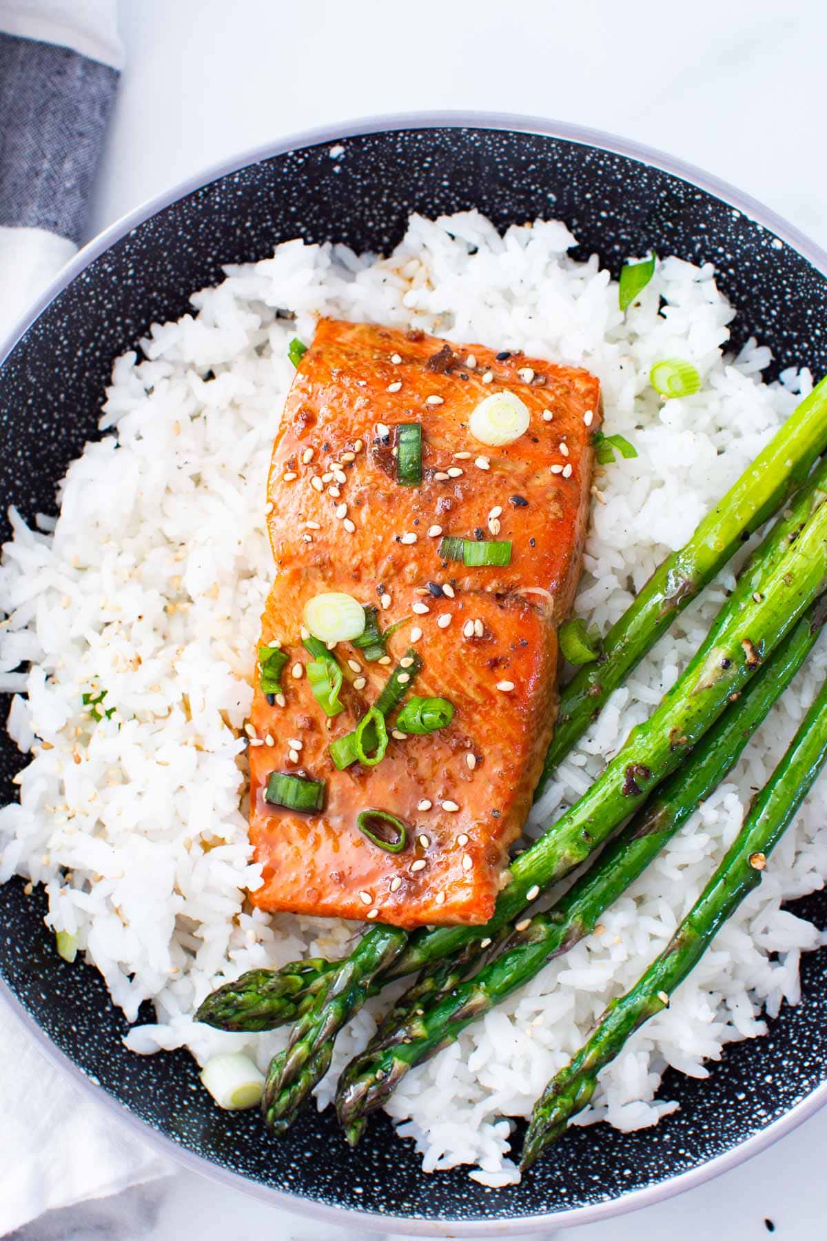 Baked teriyaki salmon plated with rice and asparagus, garnished with green onions.