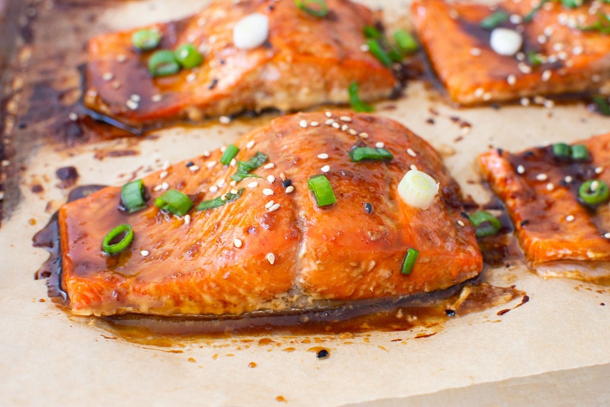 Baked teriyaki salmon with sesame seeds and green onion on baking sheet.